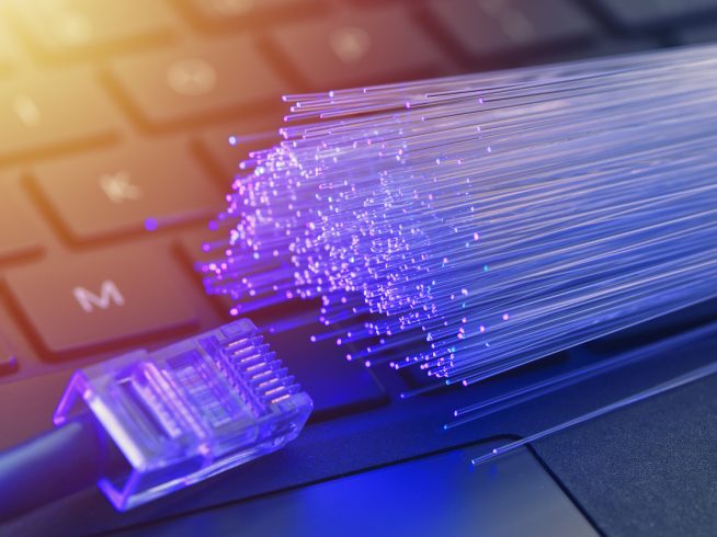 Fiber optics in blue, close up with ethernet and keyboard background, warm lens flare